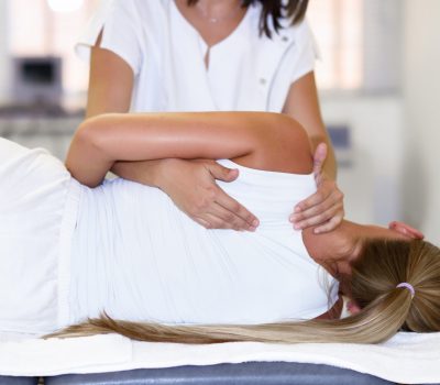 Professional female physiotherapist giving shoulder massage to blonde woman in hospital. Medical check at the shoulder in a physiotherapy center.